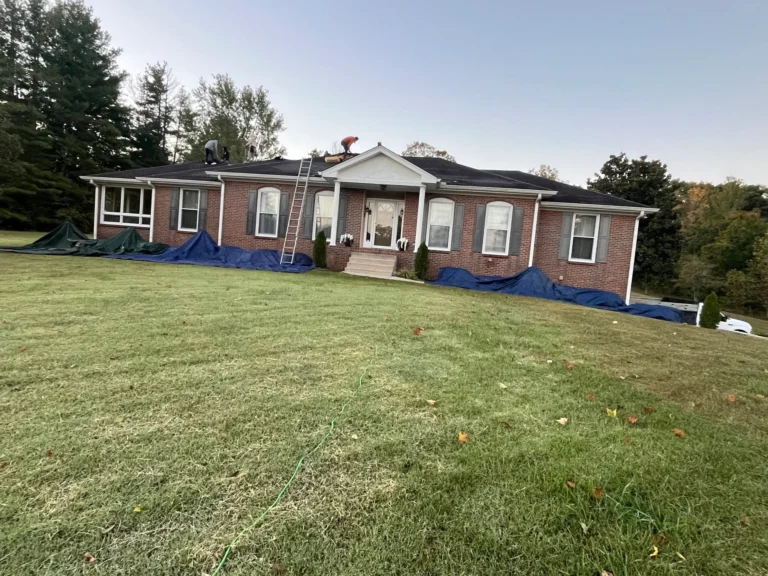 Crew working on a brick home's roof with tarps protecting the yard
